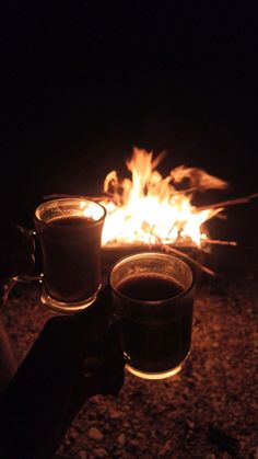 two cups of coffee sitting in front of a campfire