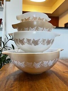 four white glass bowls stacked on top of each other in front of a potted plant