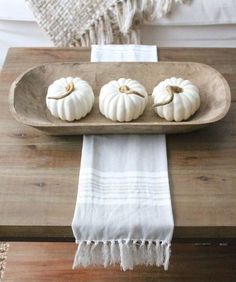 three white pumpkins sitting on a wooden tray next to a white towel and pillow