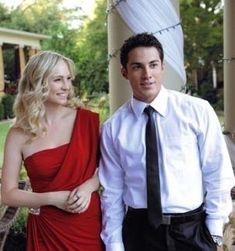 a man and woman standing next to each other in front of a gazebo wearing red dresses