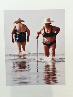 two women in swimsuits and hats are walking through the water with an oar