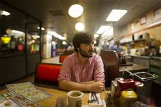 a man sitting at a table in a fast food restaurant with his arms crossed and looking off to the side