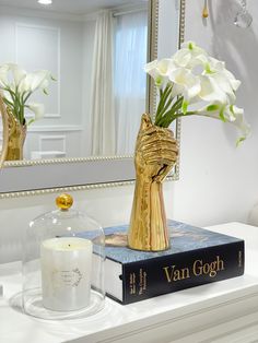 there is a vase with flowers and a candle on top of a book in front of a mirror