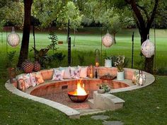 a fire pit surrounded by lots of pillows and lights in the middle of a park