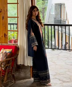 a woman standing in front of a window wearing a long black dress with colorful patterns