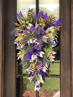 a wreath with purple and yellow ribbons hanging from the front door to welcome people into the house