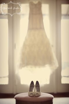 a pair of shoes sitting on top of a table next to a dress hanging from a window