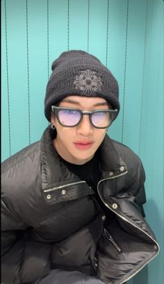 a young man wearing glasses and a beanie is posing for the camera in front of a blue wall