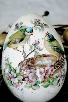 an egg with birds painted on it sitting on a table next to other eggs and flowers