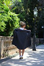 a woman walking down the street with a black blanket on her back