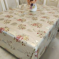 a dining room table covered with a flowered tablecloth and vase filled with flowers