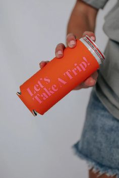 a person holding an orange can that says let's take a trip