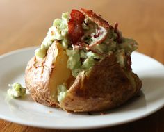 a baked potato with bacon and guacamole on it sitting on a white plate