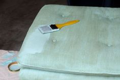 a yellow paintbrush sitting on top of a green ottoman cushion with white piping