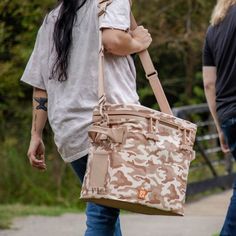 a woman with long hair carrying a brown camouflage print bag while walking down a sidewalk