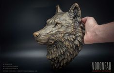 a hand is holding a bronze statue of a wolf's head on a black background