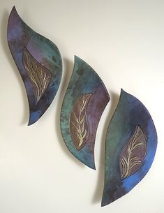 three metal leaf wall hangings mounted on a white wall next to each other with blue and purple designs