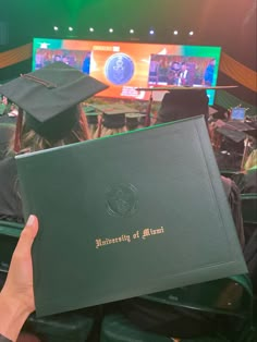 a person holding up a green book in front of a stage with people watching it