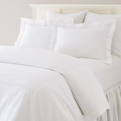 a bed with white sheets and pillows on it