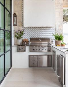 an outdoor kitchen with stainless steel appliances and white counter tops, along with potted plants