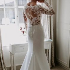 a woman in a white wedding dress is standing near a window with her hands on her head