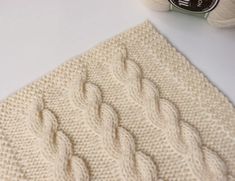 a white knitted blanket sitting on top of a table next to a ball of yarn