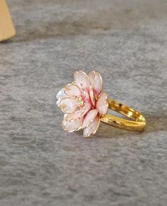 a pink flower ring sitting on top of a gray floor next to a yellow card