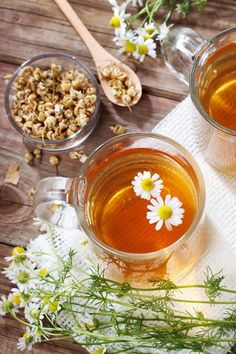 two cups of tea with chamomile and flowers on the side, next to wooden spoons