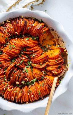 a white dish filled with cooked sweet potatoes and garnished with herbs