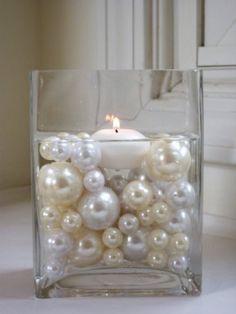 a candle that is sitting inside of a glass container filled with pearls and other things