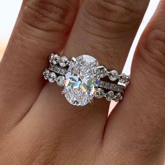 a woman's hand with a diamond ring on top of her finger and the other hand holding an engagement ring