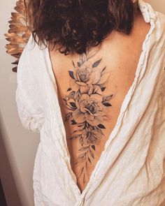 the back of a woman's neck with flowers and leaves tattooed on her chest