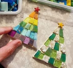 a hand is holding a small christmas tree made out of colored glass tiles and other crafting supplies