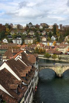 a bridge over a river with buildings on the other side and hills in the background