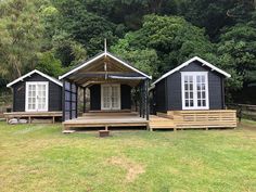 two small black cabins sitting on top of a lush green field next to trees in the background