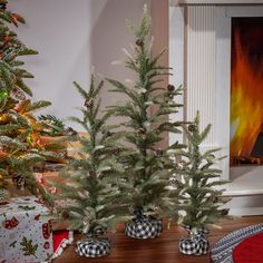 three small christmas trees sitting on top of a wooden table in front of a fireplace