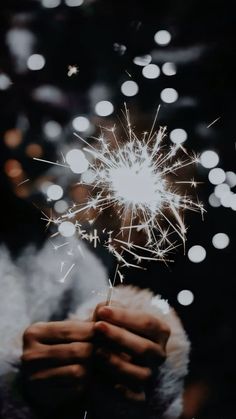 someone holding their hand in front of a firework with blurry lights behind them