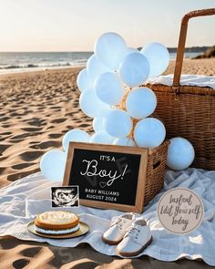 there is a basket with white balloons on the beach next to some shoes and cake