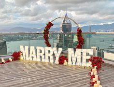 a sign that says marry me on top of a building with candles and flowers around it