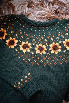 a green sweater with sunflowers on it is sitting on a furnishing