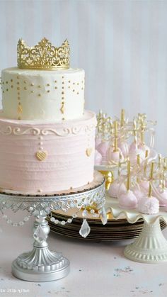 three tiered cake with pink frosting and gold crown on top, surrounded by other desserts