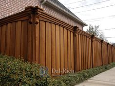 a wooden fence next to a brick building with green bushes growing on the side of it