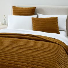 a bed with brown and white pillows on top of it, next to a night stand