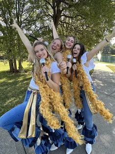 three girls in blue jeans and yellow feathered dresses are posing for the camera with their arms up