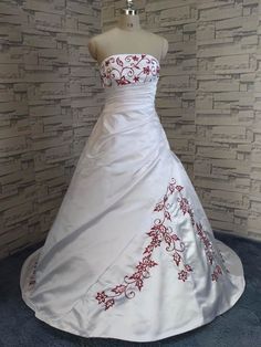 a white wedding dress with red flowers on the bustle and underskirt, sitting on a mannequin in front of a brick wall