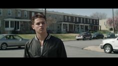 a young man standing in the middle of a street with cars parked on both sides