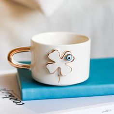 a white coffee cup with a four leaf clover on it and a blue book next to it