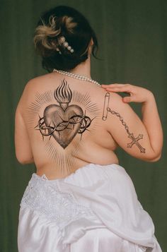 the back of a woman with tattoos on her upper and lower back, in a white dress