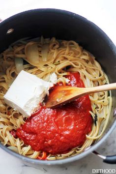 a pot filled with pasta and sauce on top of a white counter next to a wooden spoon