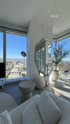 a living room filled with white furniture and large windows overlooking the cityscape in the distance